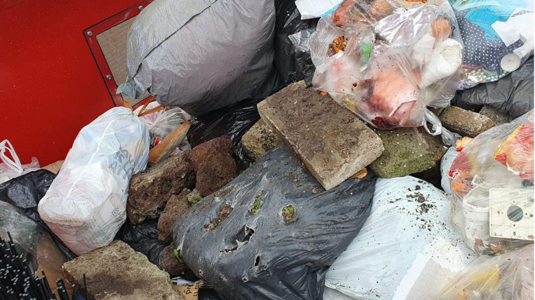 Schade aan vuilniswagen door stenen en tegels tussen restafval